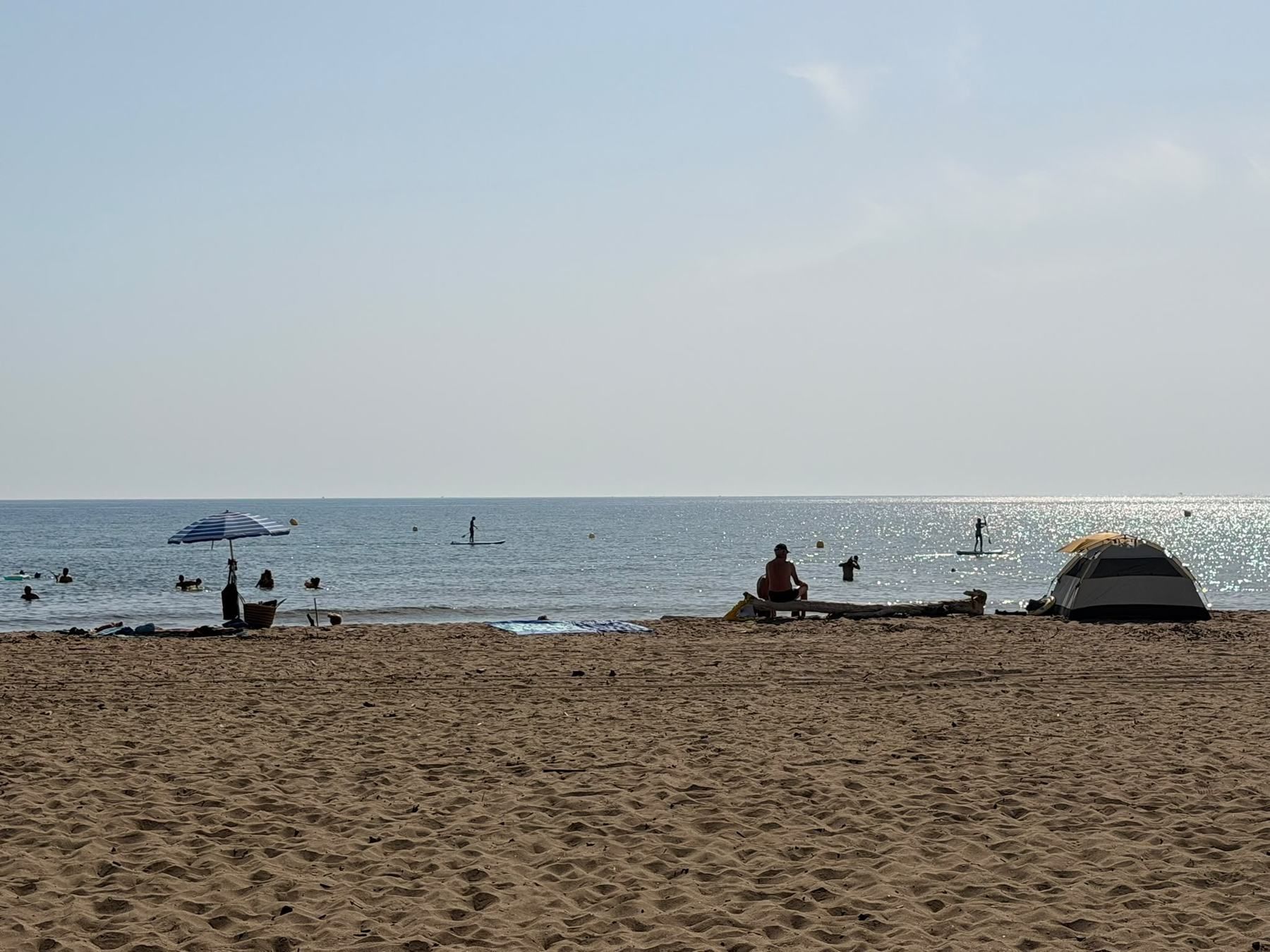 Sandy Costa Brava beach with swimmers and a parasol by the sea