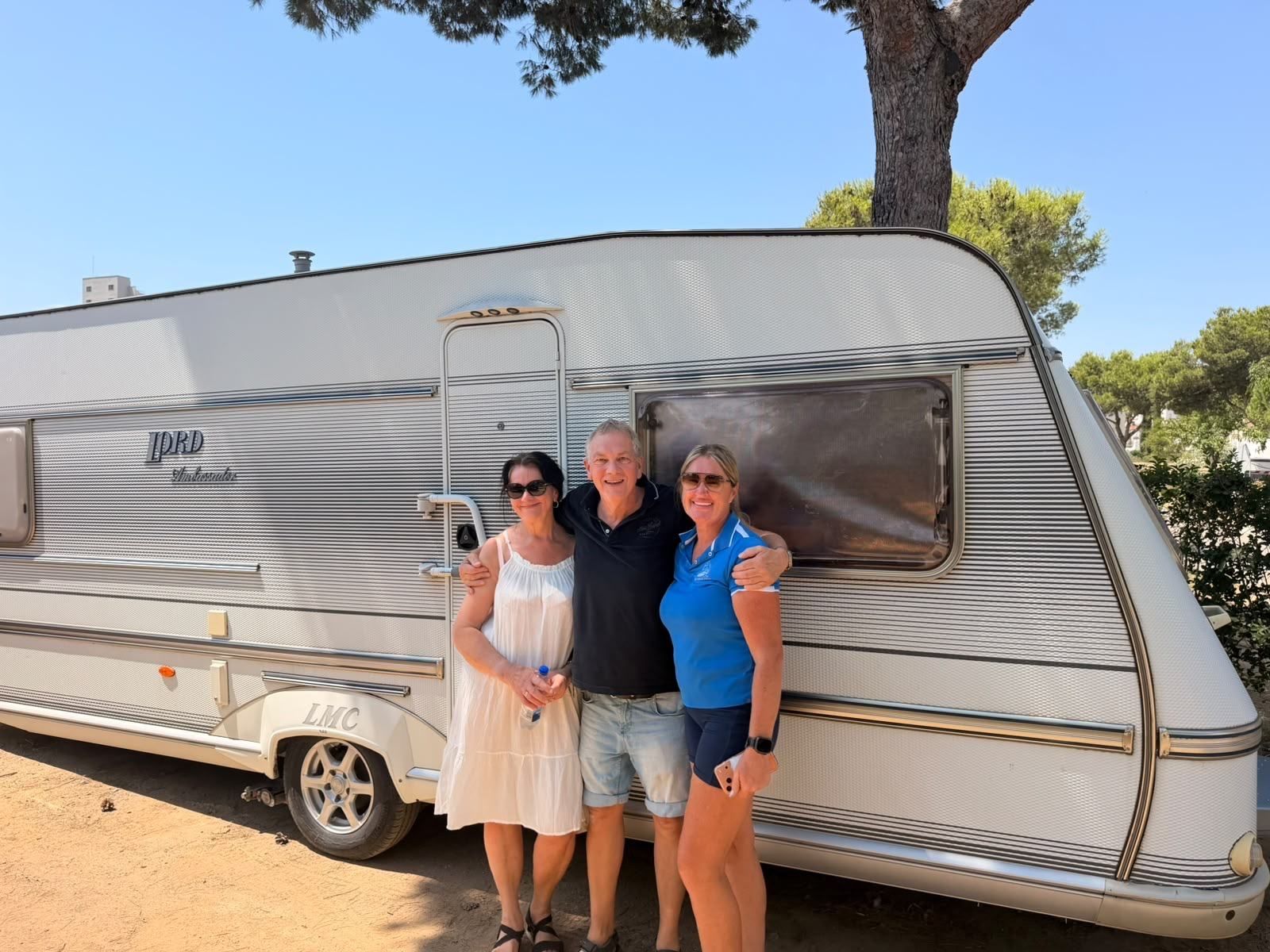 Three people smiling in front of an LMC caravan