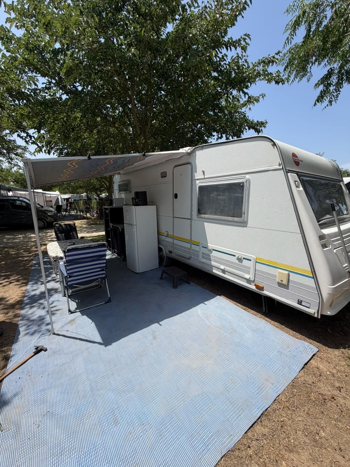 Caravan with a roll-out awning and groundsheet under a tree