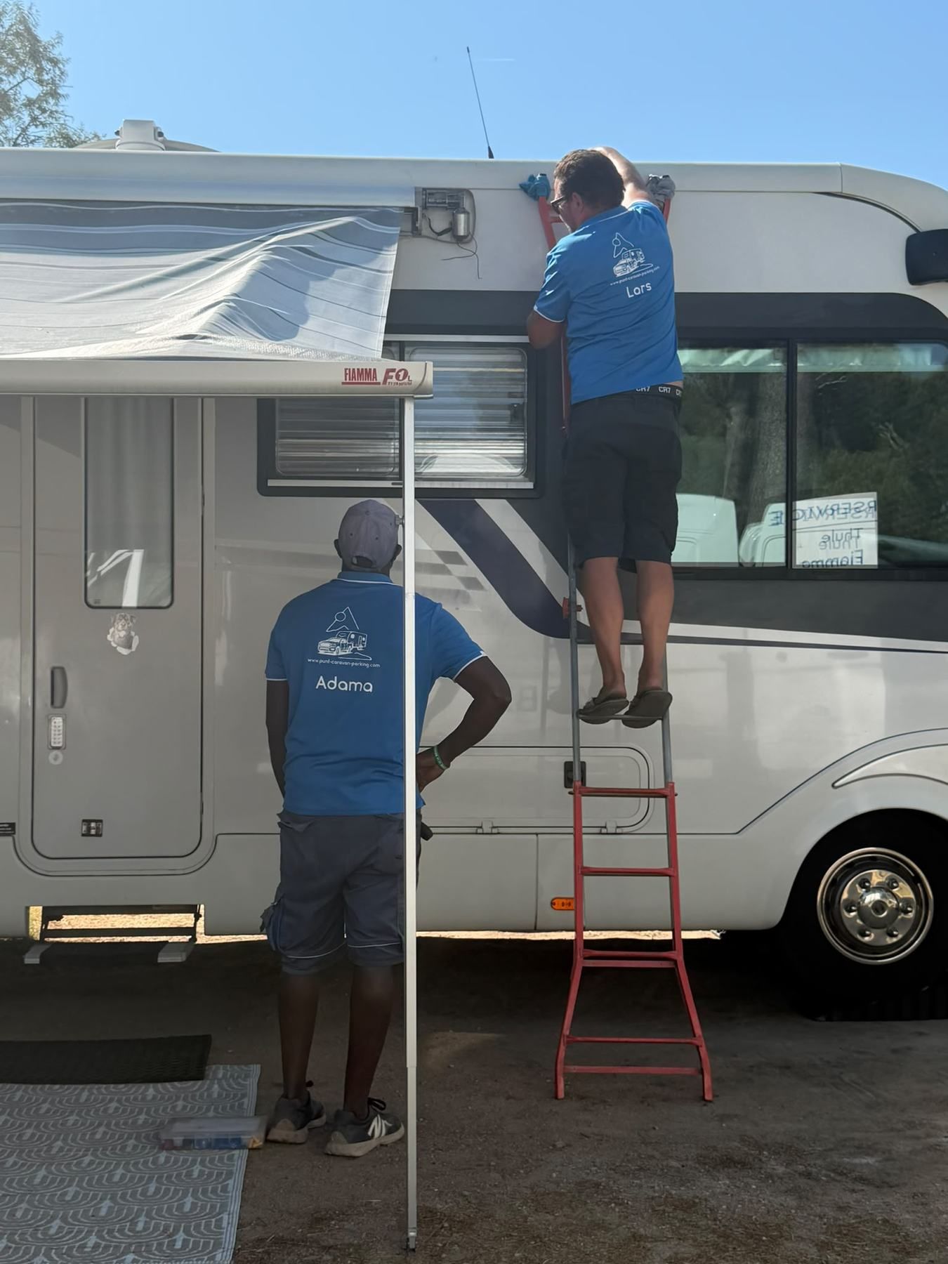 Two team members on a ladder fitting a roll-out awning to a motorhome