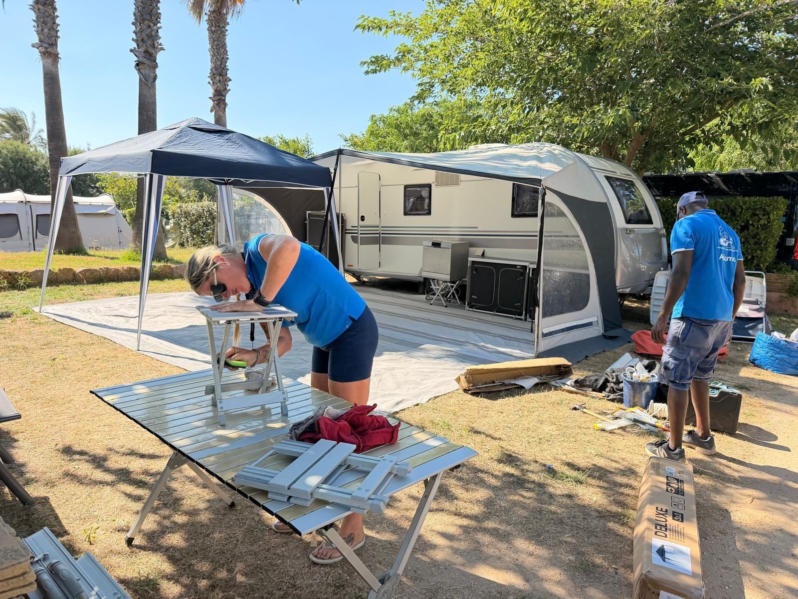 Team member assembling a camping table beside a caravan under a gazebo