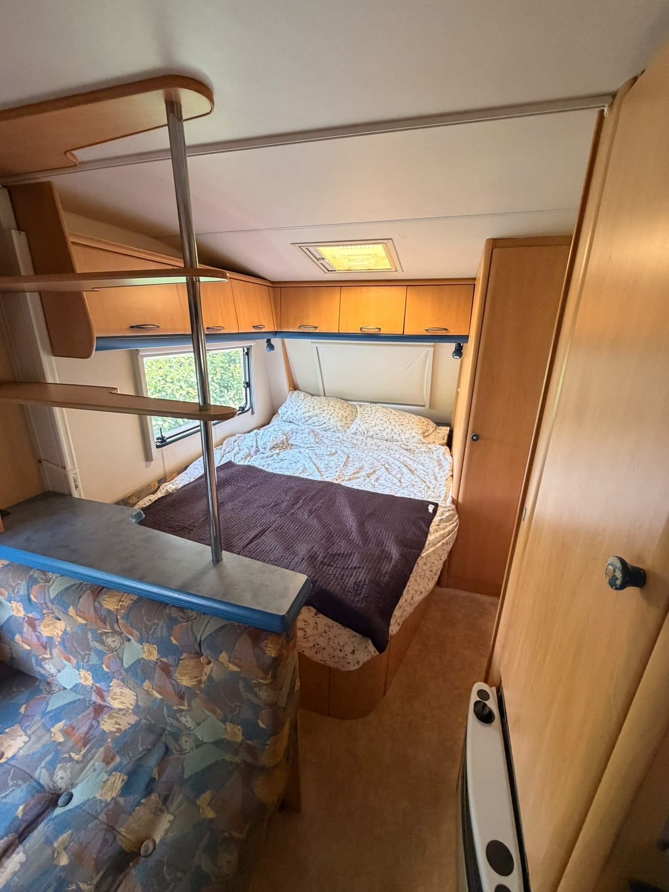 Caravan interior with a made-up double bed and wooden cupboards