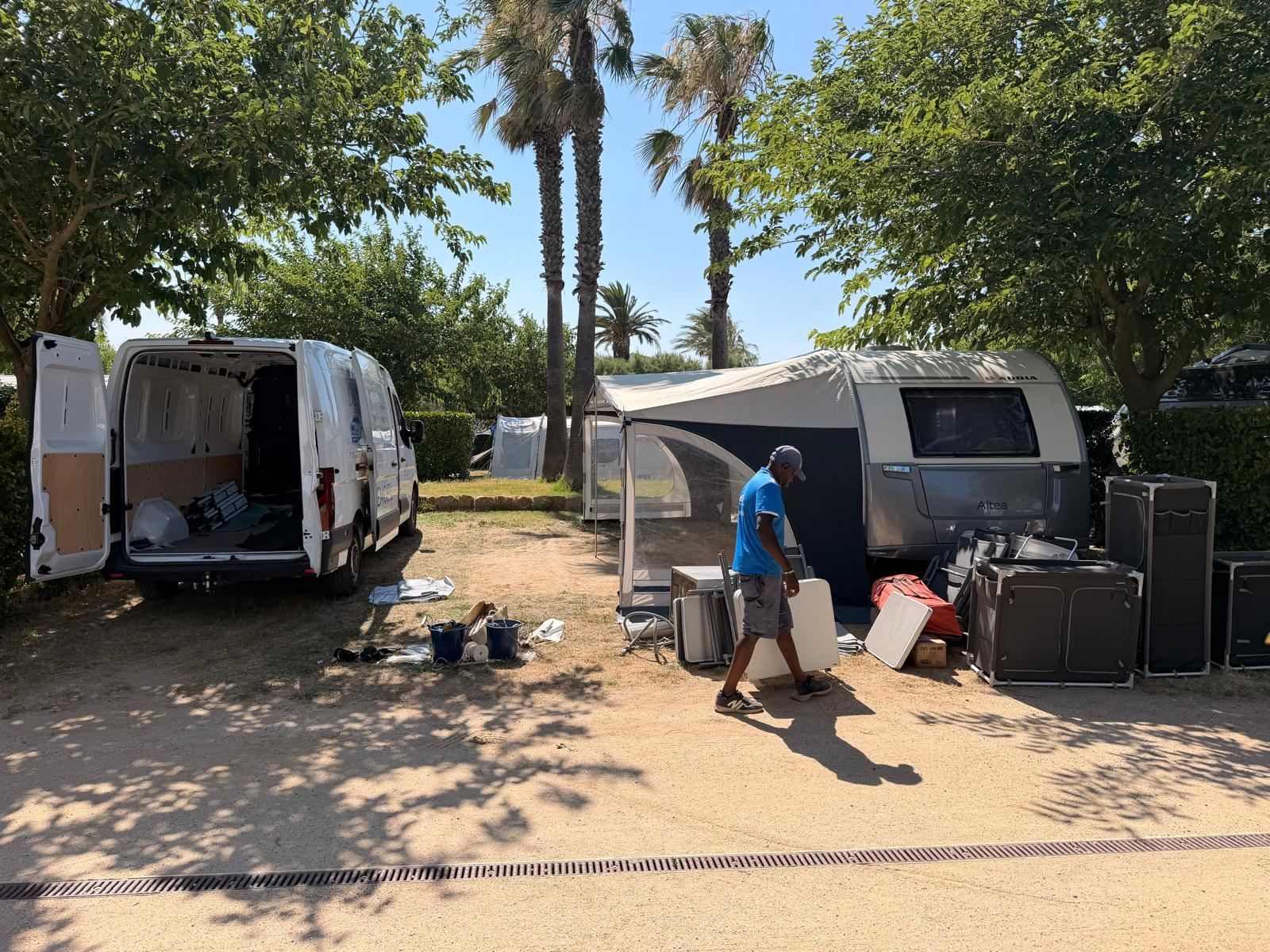 Team member carrying awning parts to a caravan on a shaded pitch