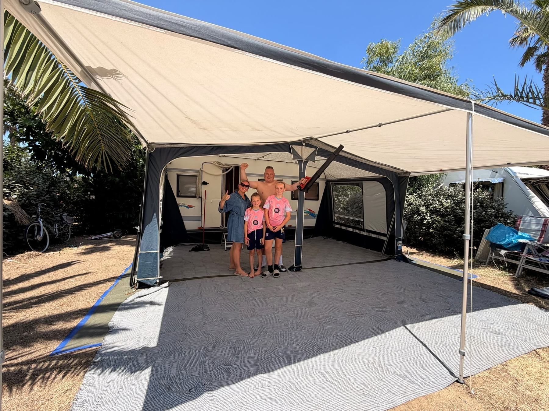 Family standing under the roll-out awning of their caravan