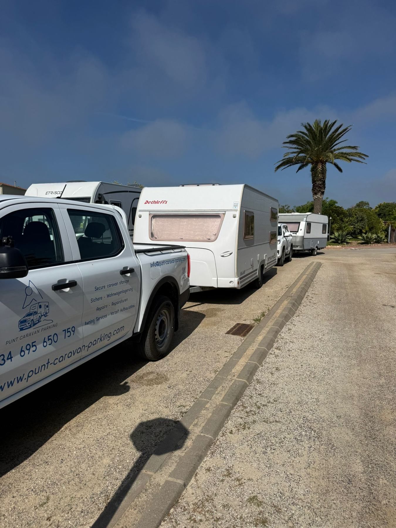 Punt pickup with the company phone number on the door, caravans lined up along a campsite road