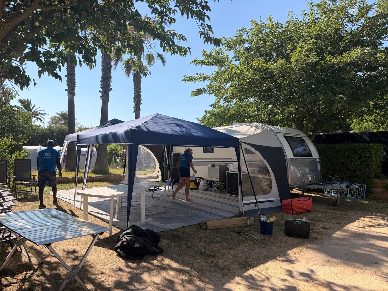 Two team members putting up a gazebo and awning floor next to a caravan