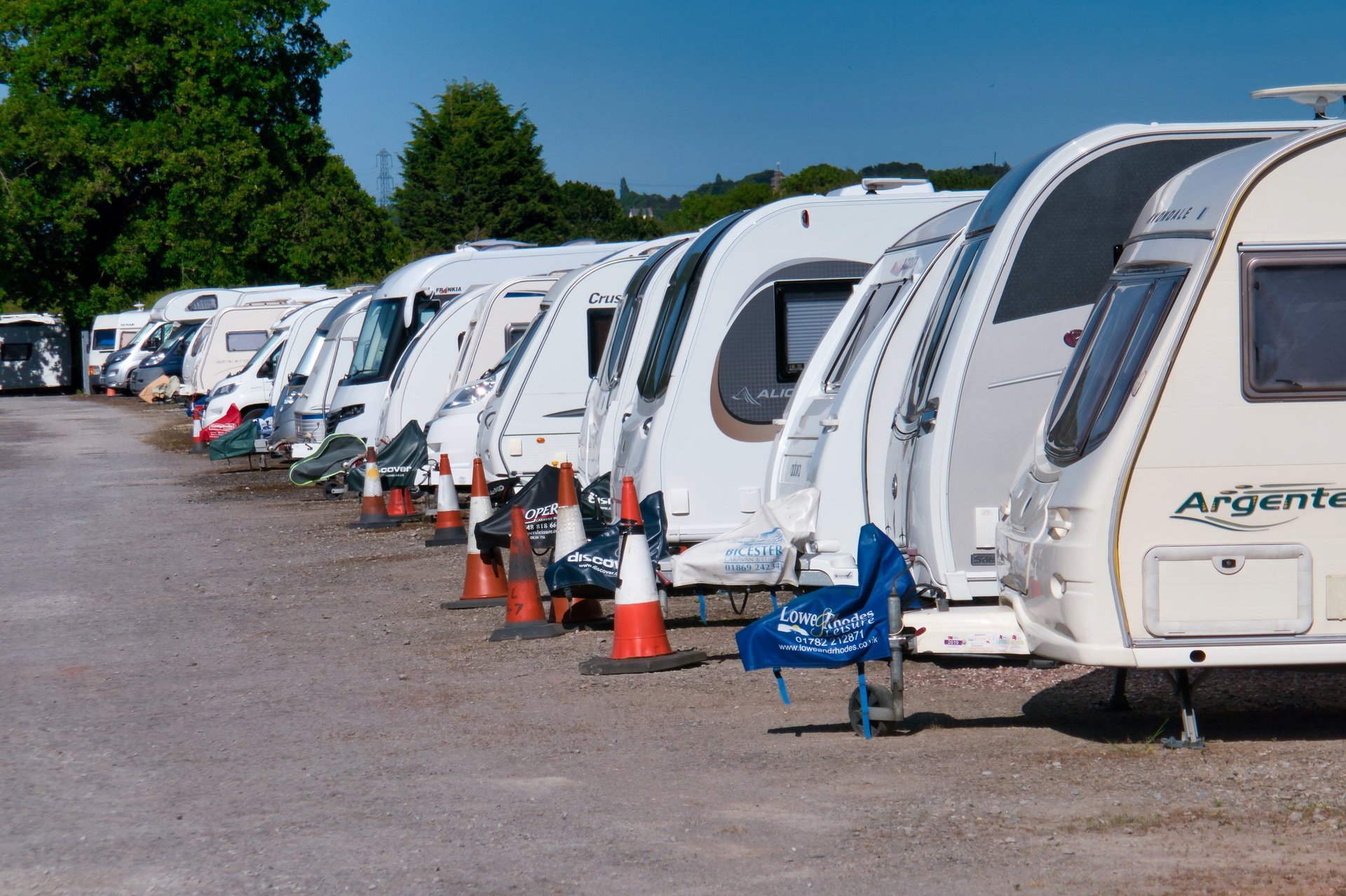 Een rij witte caravans op een verharde ondergrond in een beveiligde caravanstalling op een zonnige zomerdag met blauwe lucht.