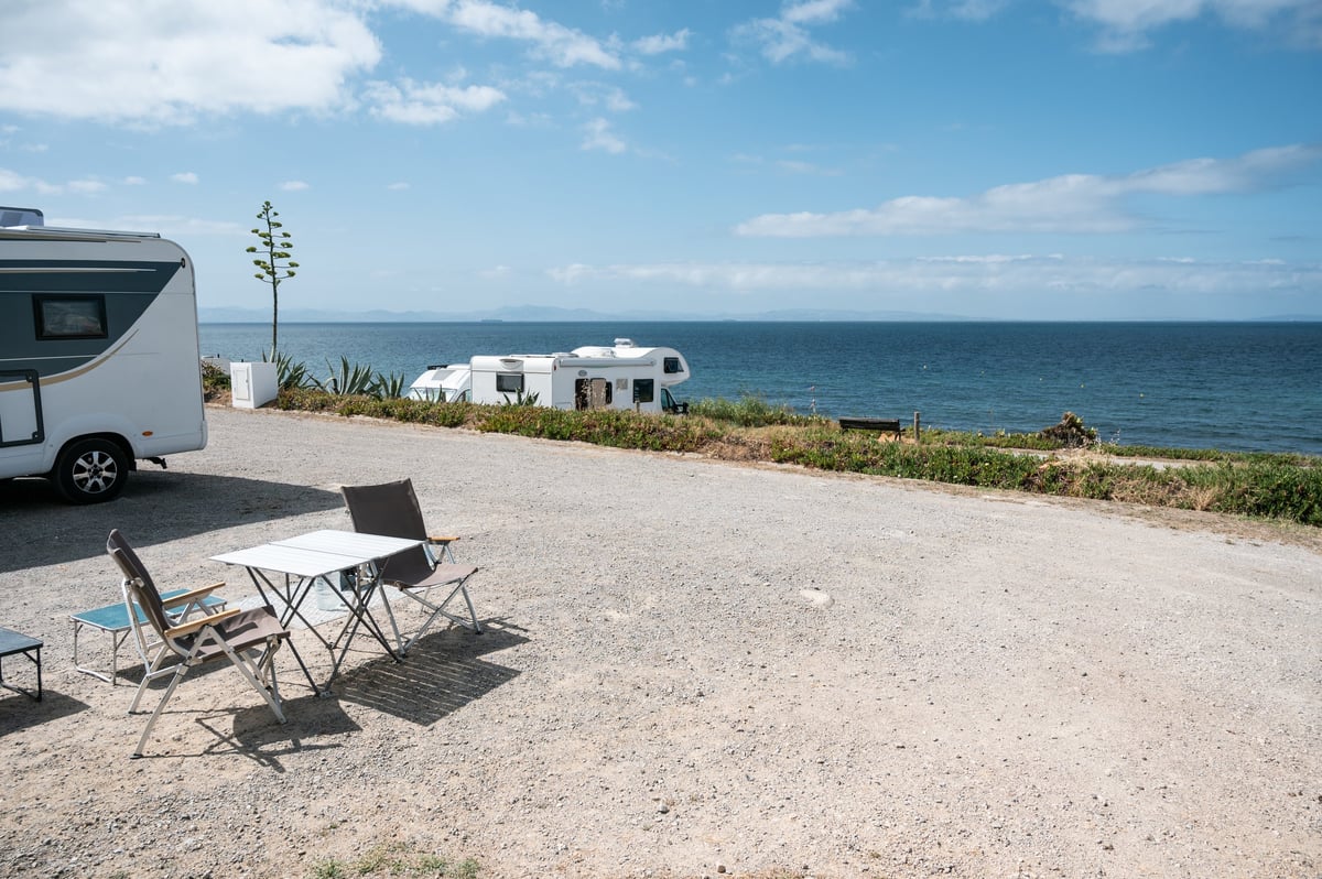 Campers enjoying ocean view from their campsite with RVs and camping chairs during a sunny day